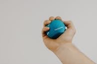 Crop unrecognizable male athlete with small rubber ball in hand exercising during recovery process on light background