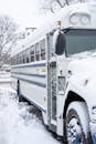 A snow-covered school bus parked outdoors in a winter landscape with bare trees.